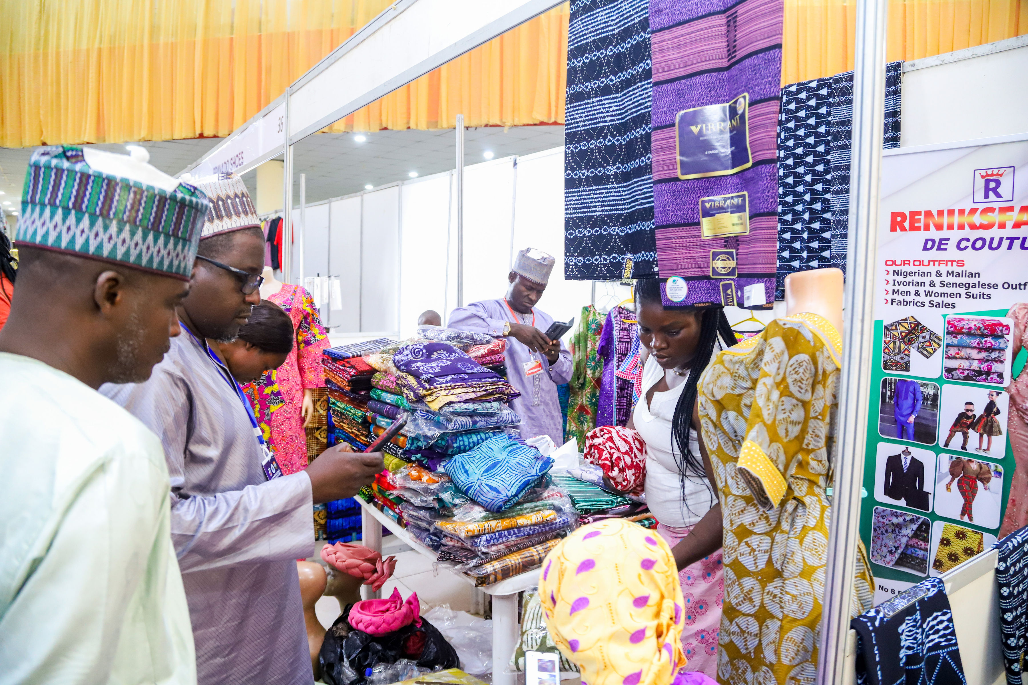 Buyers browsing vibrant Nigerian and African fabric collections at a vendor booth inside the UI SME Fair exhibition hall